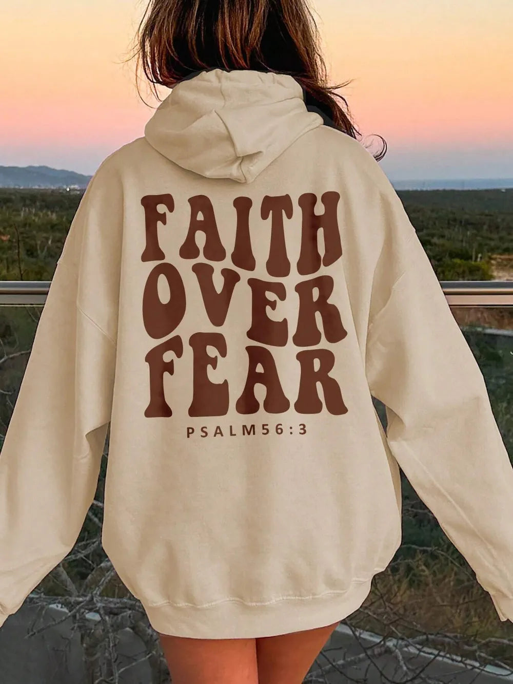 Person wearing a beige hoodie with 'Faith Over Fear' text at sunset