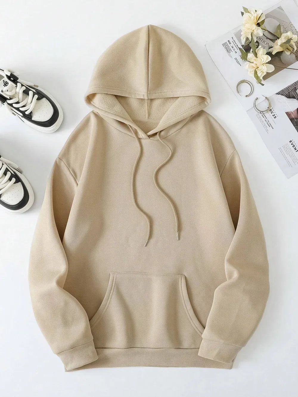Beige hoodie on a white surface with sneakers and flowers in the background