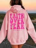 Person wearing a pink hoodie with 'Faith Over Fear' text outdoors.