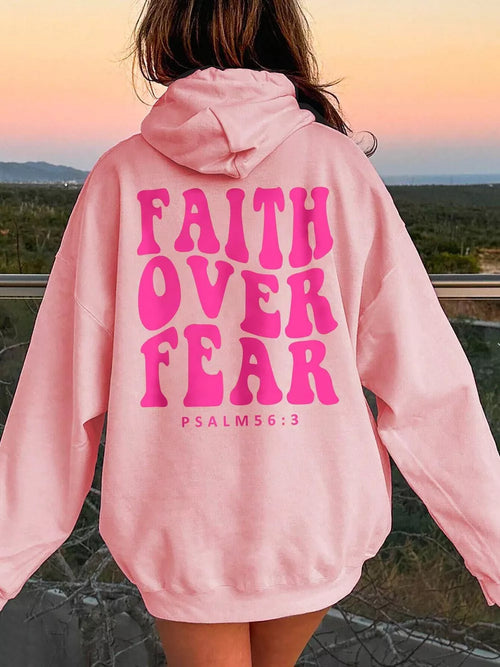 Person wearing a pink hoodie with 'Faith Over Fear' text outdoors.
