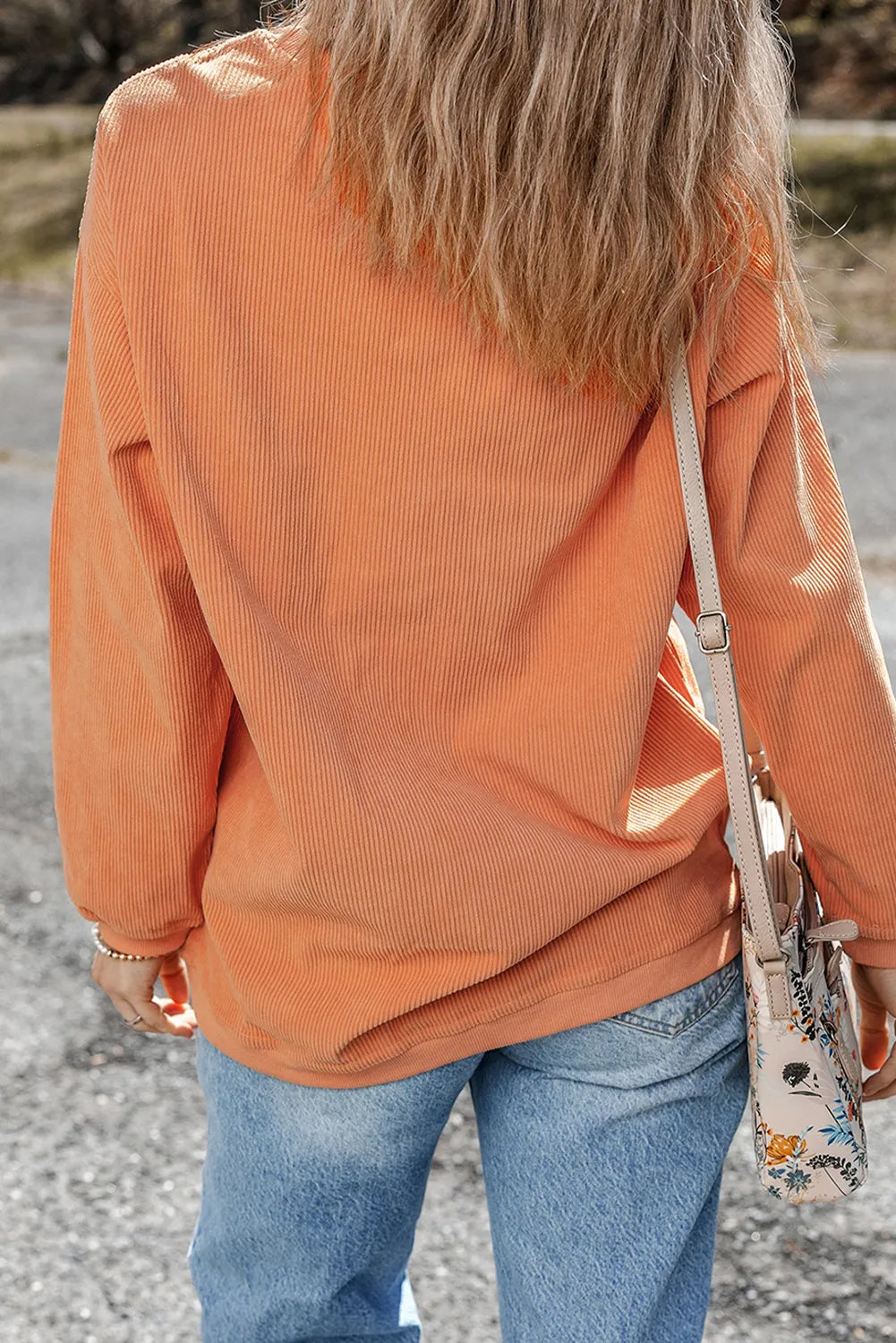 Woman wearing a pumpkin-orange ribbed sweatshirt with white “thankful.” lettering, styled with light-wash jeans