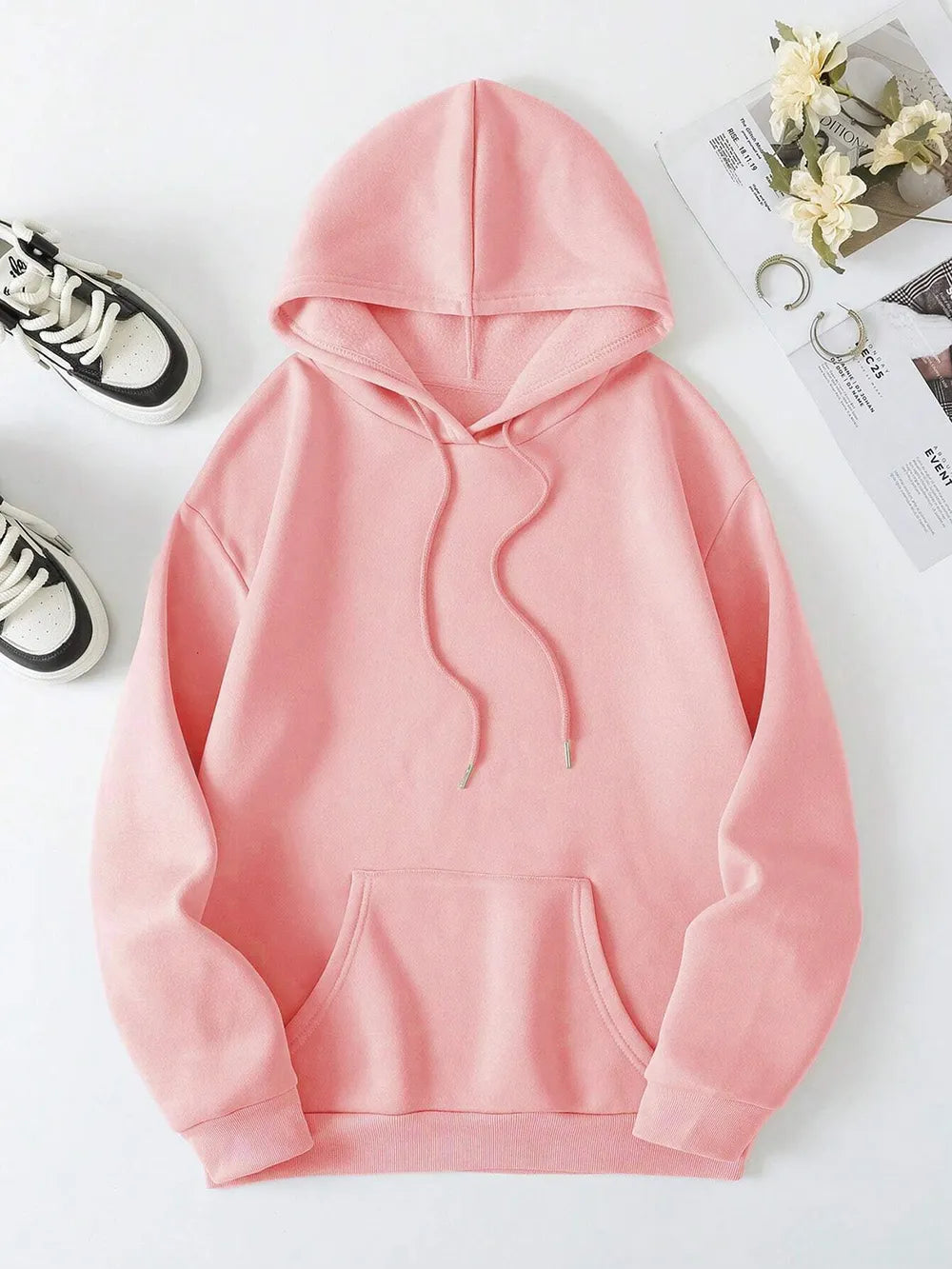 Pink hoodie on a white surface with shoes and flowers in the background