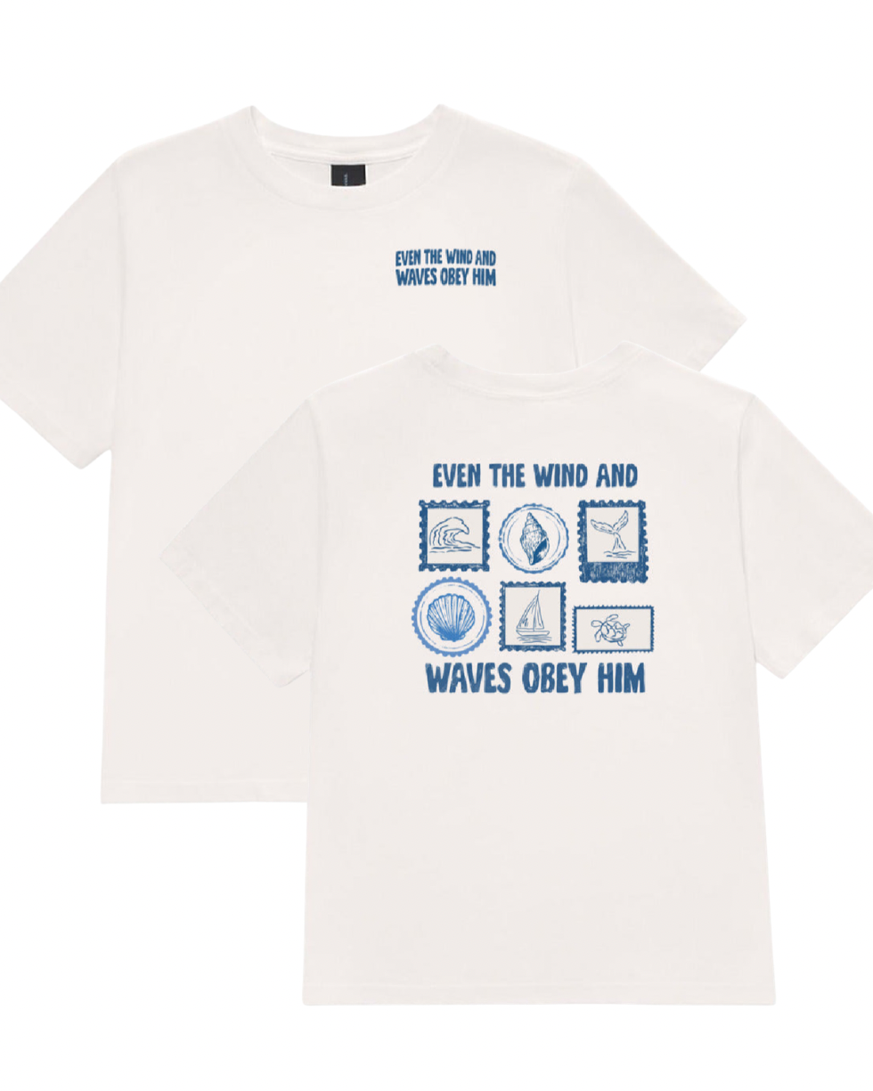 Two white short-sleeve t-shirts shown on a plain white background, with the front and back views overlapping. The shirts feature a blue graphic print with nautical icons and the text 'EVEN THE WIND AND WAVES OBEY HIM' on the front, and a smaller matching text print on the back.