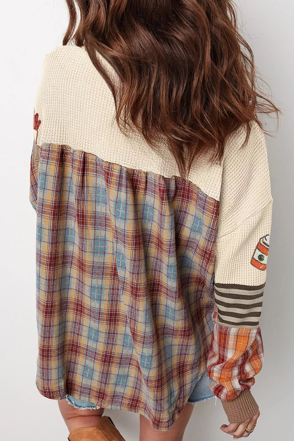 Woman wearing a cream waffle knit top with sequin autumn leaves and coffee cups, a striped button neckline, and orange plaid sleeve panels