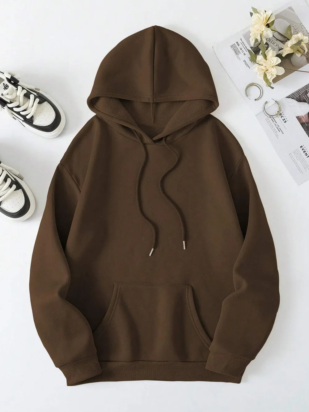 Brown hoodie on a white surface with shoes and flowers in the background