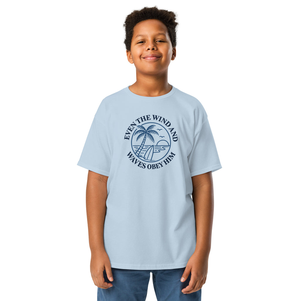 light blue Christian T-shirt with a navy palm tree, surfboard, and ocean graphic surrounded by “Even the wind and waves obey Him“