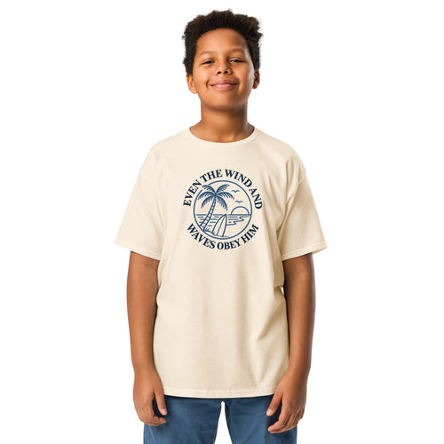 Beige Christian T-shirt with a navy palm tree, surfboard, and ocean graphic surrounded by “Even the wind and waves obey Him